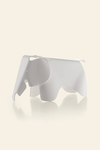 The Vitra Eames Elephant, Small by Vitra is a minimalist, white, abstract decorative piece with a smooth finish, shaped like an elephant and set against a light beige background with a gentle reflection beneath it.
