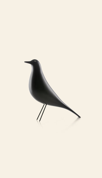 The Vitra Eames House Bird by Vitra features a minimalist design with a smooth black finish, standing upright on slender legs—a timeless decor piece shown against a plain, light beige background.