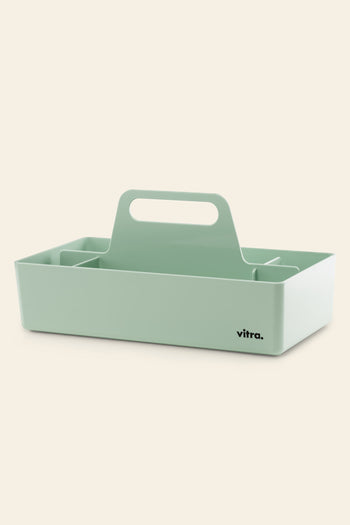 A light green Vitra Toolbox RE table caddy by Vitra, rectangular with a central handle and multiple compartments, made from recycled ABS plastic and featuring a black vitra. logo on one corner, set against a plain beige background.