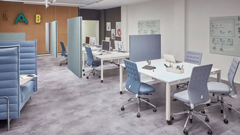 Modern, open office with light blue chairs, white desks with computers, Vitra partition screens, and whiteboards on the walls. A colorful LAB sign shines in the background, and Vitras Toolbox RE tables made from recycled ABS plastic complete the scene.