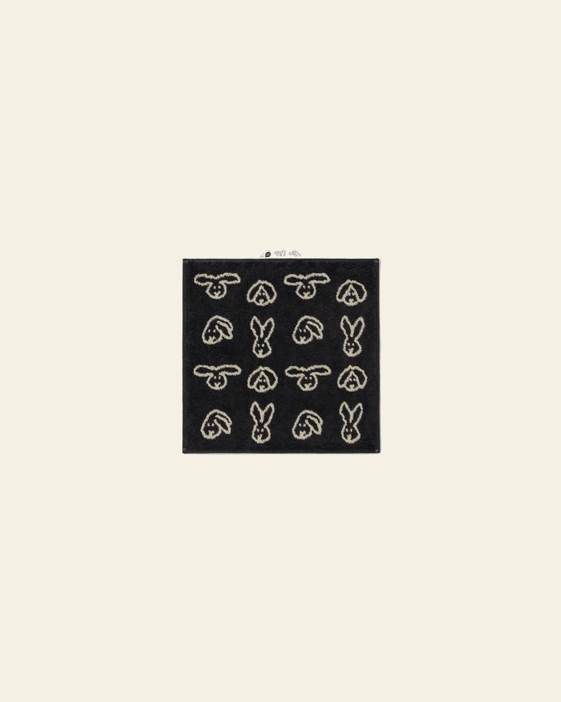 The WARMGREY TAIL Bunny Bunny Hand Towel by WARMGREY TAIL is a black rectangular hand towel featuring a grid of white bunny head outlines, shown against a light beige background.