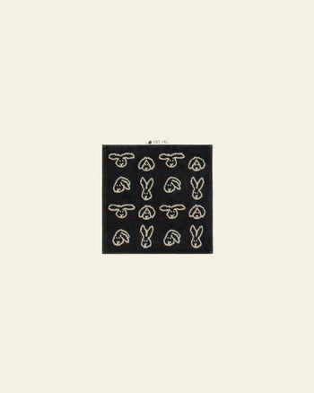 The WARMGREY TAIL Bunny Bunny Hand Towel by WARMGREY TAIL is a black rectangular hand towel featuring a grid of white bunny head outlines, shown against a light beige background.