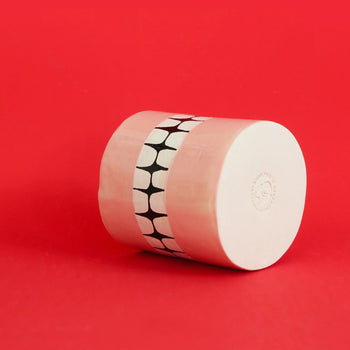 The Wobbly Studio Denture Pot, a cylindrical ceramic piece with a pink and white finish and central black-and-white geometric band, rests on its side against a bright red background.