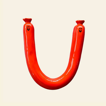 The Wobbly Studio Happy Saucisse Wall Decor features a red, U-shaped sausage with smiling faces on each end, bringing a playful and cheerful vibe to your space.