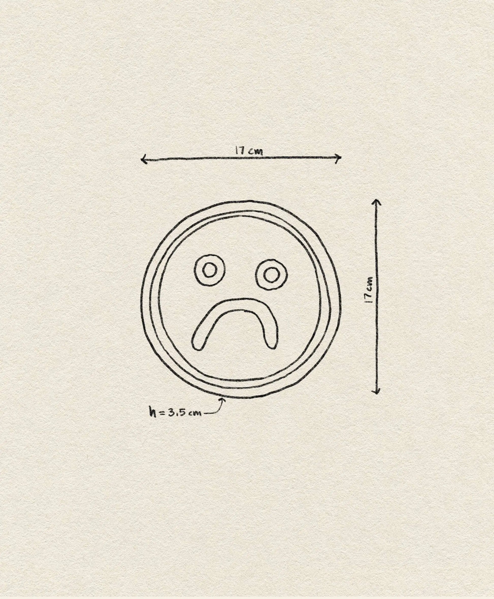 The Wobbly Studio Mood Tray by Wobbly Studio features a simple black sad face line drawing on a circular tray (17cm diameter, 3.5cm height) set against a beige textured background—perfect for adding personality to your space.