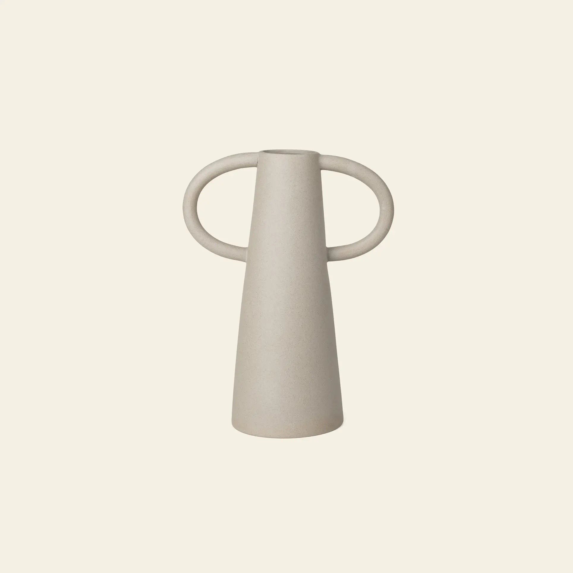 The ferm LIVING Anse Vase is a minimalist, light beige ceramic piece with a conical form and two large circular handles, crafted using traditional techniques and photographed against an off-white background.