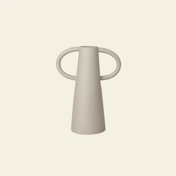 The ferm LIVING Anse Vase is a minimalist, light beige ceramic piece with a conical form and two large circular handles, crafted using traditional techniques and photographed against an off-white background.