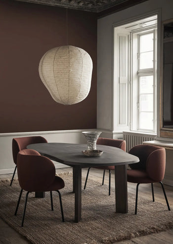 A modern dining room with a dark oval table, four reddish-brown upholstered chairs, a large paper lantern pendant light, and the ferm LIVING Blend Vase, Large by ferm LIVING on a textured rug near a tall window with white shutters.