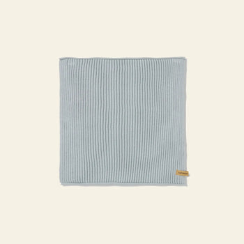 A set of seven neatly folded ferm LIVING Day Cloths, made from GOTS-certified organic cotton in light blue with a small brown tag, is displayed on a plain beige background.