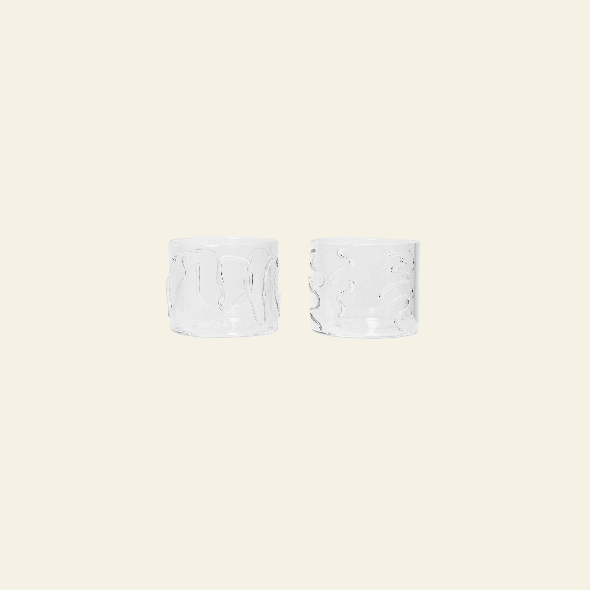 The ferm LIVING Doodle Glasses Low, Set of 2, made from borosilicate glass and featuring unique wavy patterns, are placed side by side on a plain light beige background.