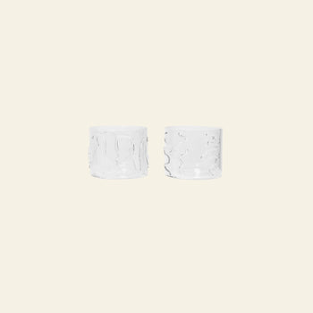 The ferm LIVING Doodle Glasses Low, Set of 2, made from borosilicate glass and featuring unique wavy patterns, are placed side by side on a plain light beige background.