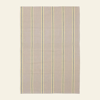 The ferm LIVING Hale Tea Towel by ferm LIVING features a rectangular beige fabric with evenly spaced vertical blue and yellow stripes, shown flat on a light background.