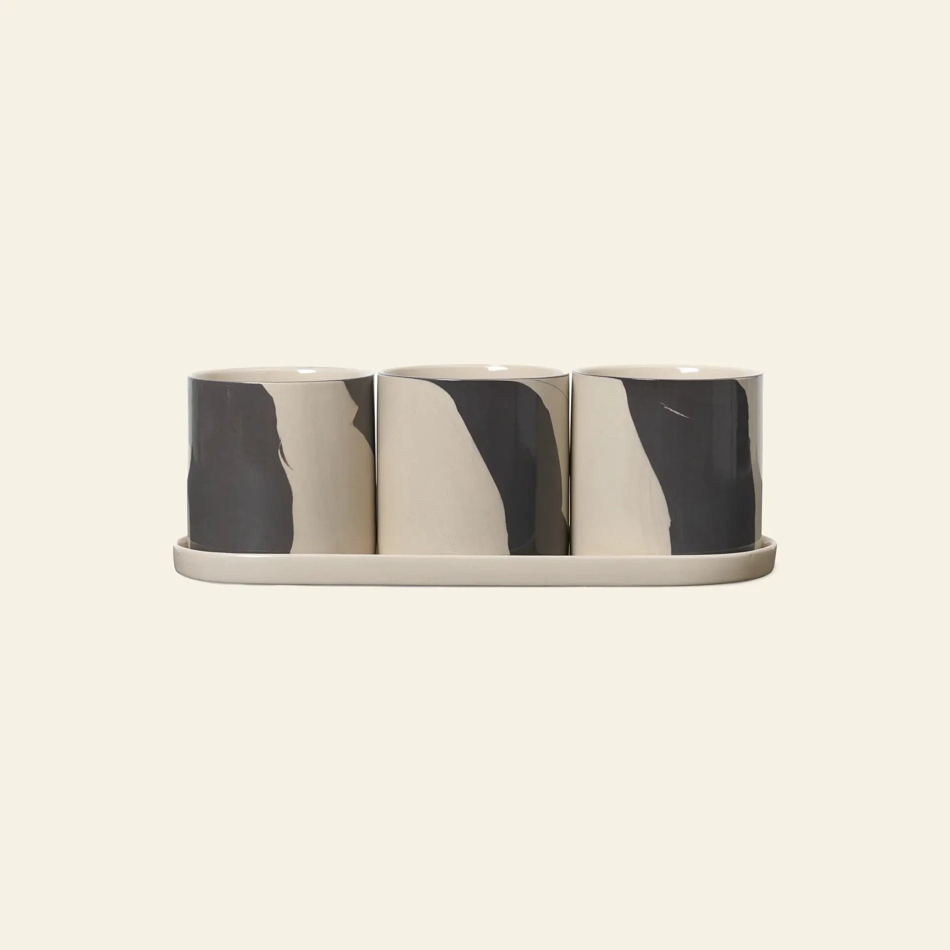 The ferm LIVING Inlay Herb Pots set includes three cylindrical stoneware planters with abstract dark gray brushstrokes on a matching tray, each with drainage holes for healthy roots.