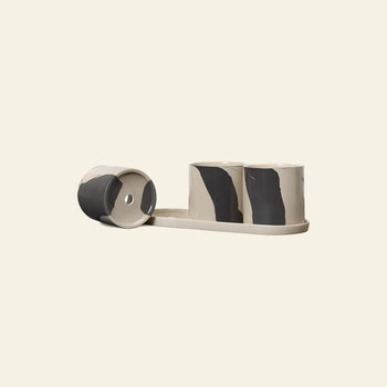 The ferm LIVING Inlay Herb Pots set includes three small cylindrical stoneware planters with black and beige patterns on an oval tray; one lies tipped to show drainage holes, all against a plain light cream background.