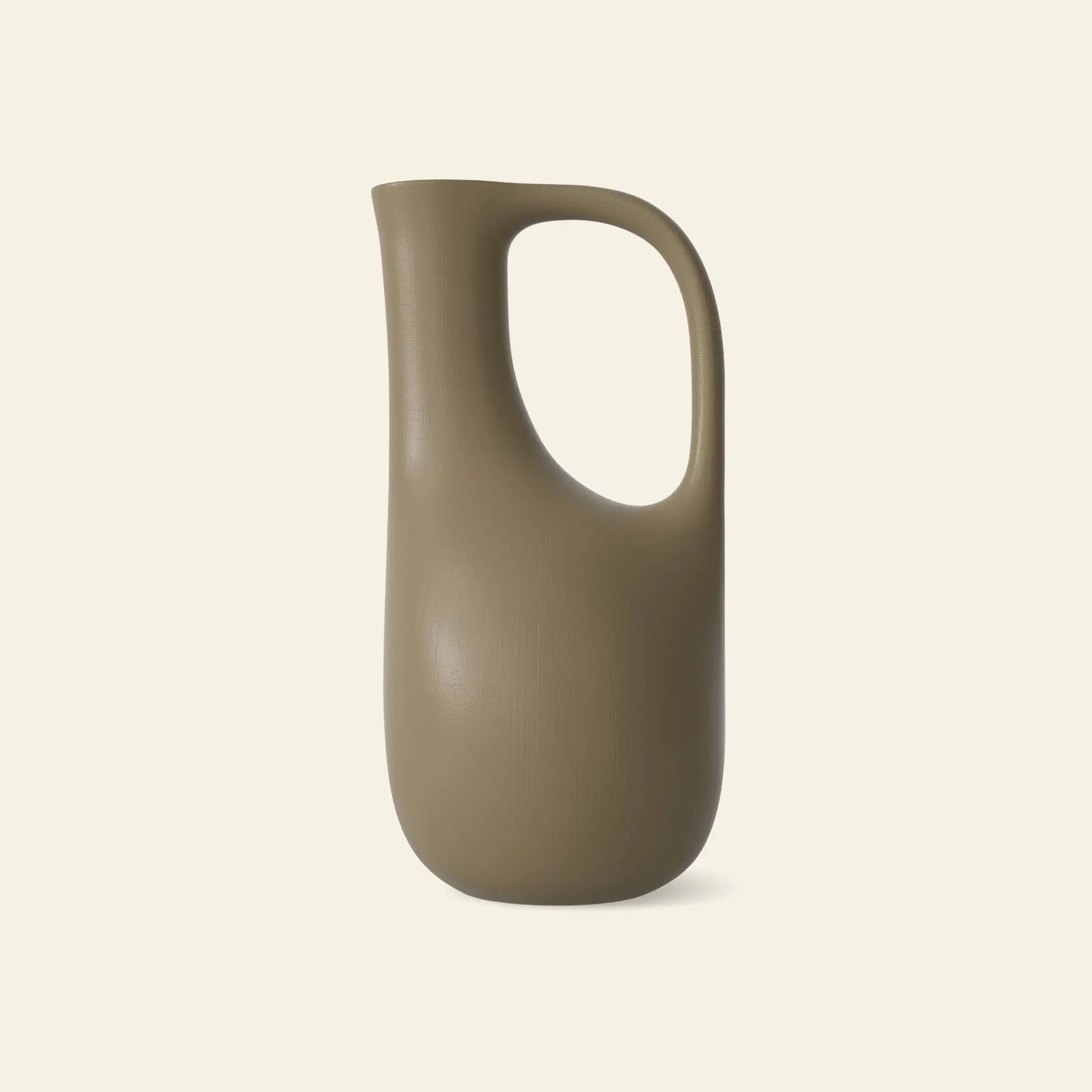 The ferm LIVING Liba Watering Can is a modern, matte beige oval-shaped pitcher with a large curved handle, crafted from recycled plastic and offering ample capacity. Set against a plain light background.