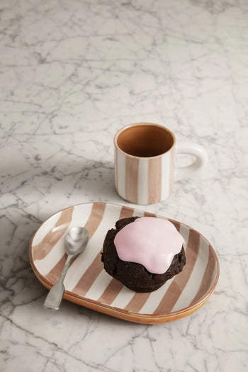 A glazed stoneware plate from the ferm LIVING Milu Snack Set holds a chocolate muffin with pink icing and a spoon on marble, while behind it sits the matching hand-painted mug by ferm LIVING filled with a dark beverage.