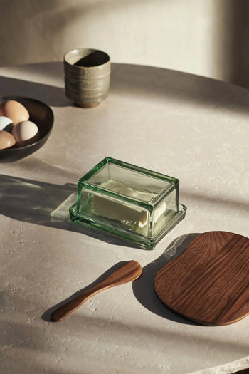 The ferm LIVING Oli Box is a versatile recycled glass container, shown here on a light surface beside kitchen essentials in soft sunlight. It’s dishwasher safe for easy cleaning.