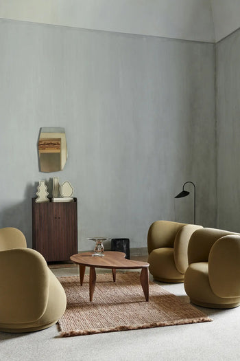A modern living room features three curved mustard chairs, a wooden coffee table, and a textured rug on neutral carpet. The ferm LIVING Paste Vase, Curvy sits on the small cabinet beneath a geometric mirror on the pale gray wall.