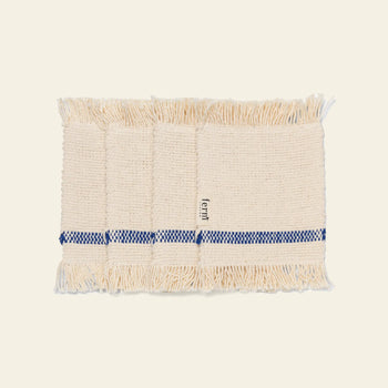 The ferm LIVING Savor Coasters, Set of 4, are beige woven coasters with fringed edges, each featuring a blue checkered stripe on one side and a small ferm label.