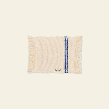 A set of four cream-colored woven ferm LIVING Savor Coasters, each rectangular with fringed edges, a blue geometric stripe near one edge, and a small fabric label reading fernt, displayed on a plain light background.