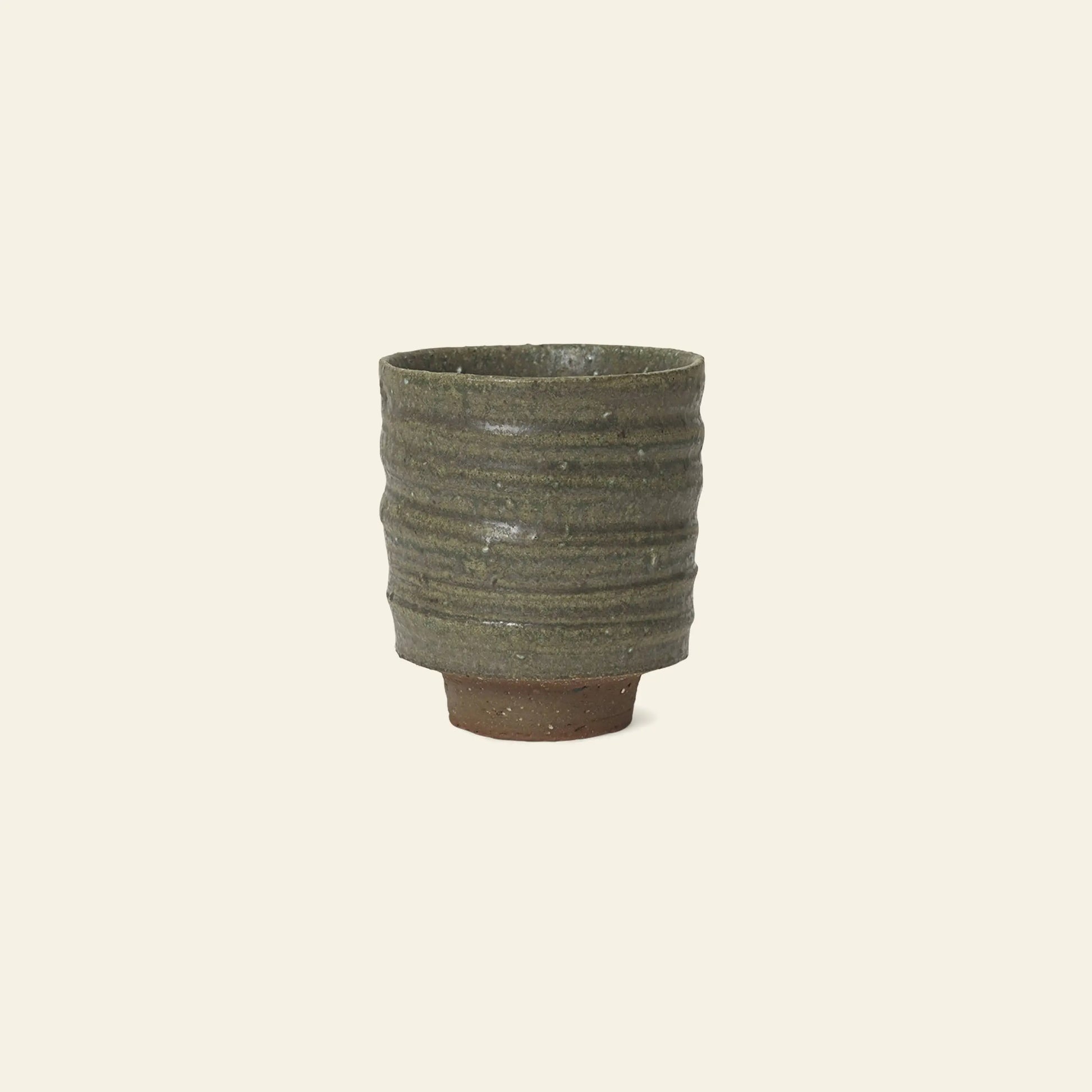The ferm LIVING Serena Cup by ferm LIVING is a handcrafted clay cup with a ribbed, textured surface in earthy green and a reactive glaze, featuring a slightly raised base against a plain light background.