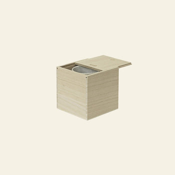 A lightweight, reusable wooden box with a sliding lid, partially open to reveal the ferm LIVING Serena Cup—a handcrafted clay cup with a gray reactive glaze—set against a plain light background.