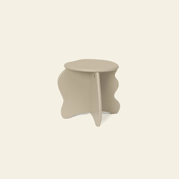 The ferm LIVING Slope Stool is a small, beige side table with a round top and sculptural wavy legs, crafted from FSC certified MDF—an organic yet modern piece by ferm LIVING, shown against an off-white background.
