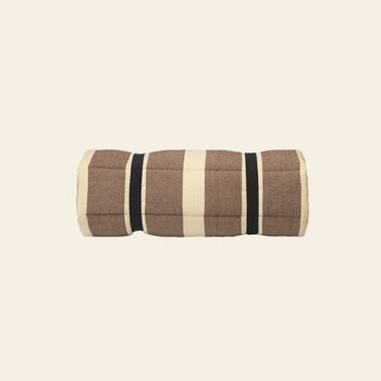 The ferm LIVING Strand Quilted Mattress by ferm LIVING is a rolled-up, brown and beige plaid blanket made from recycled polyester, secured with two black straps and displayed against a plain cream background.