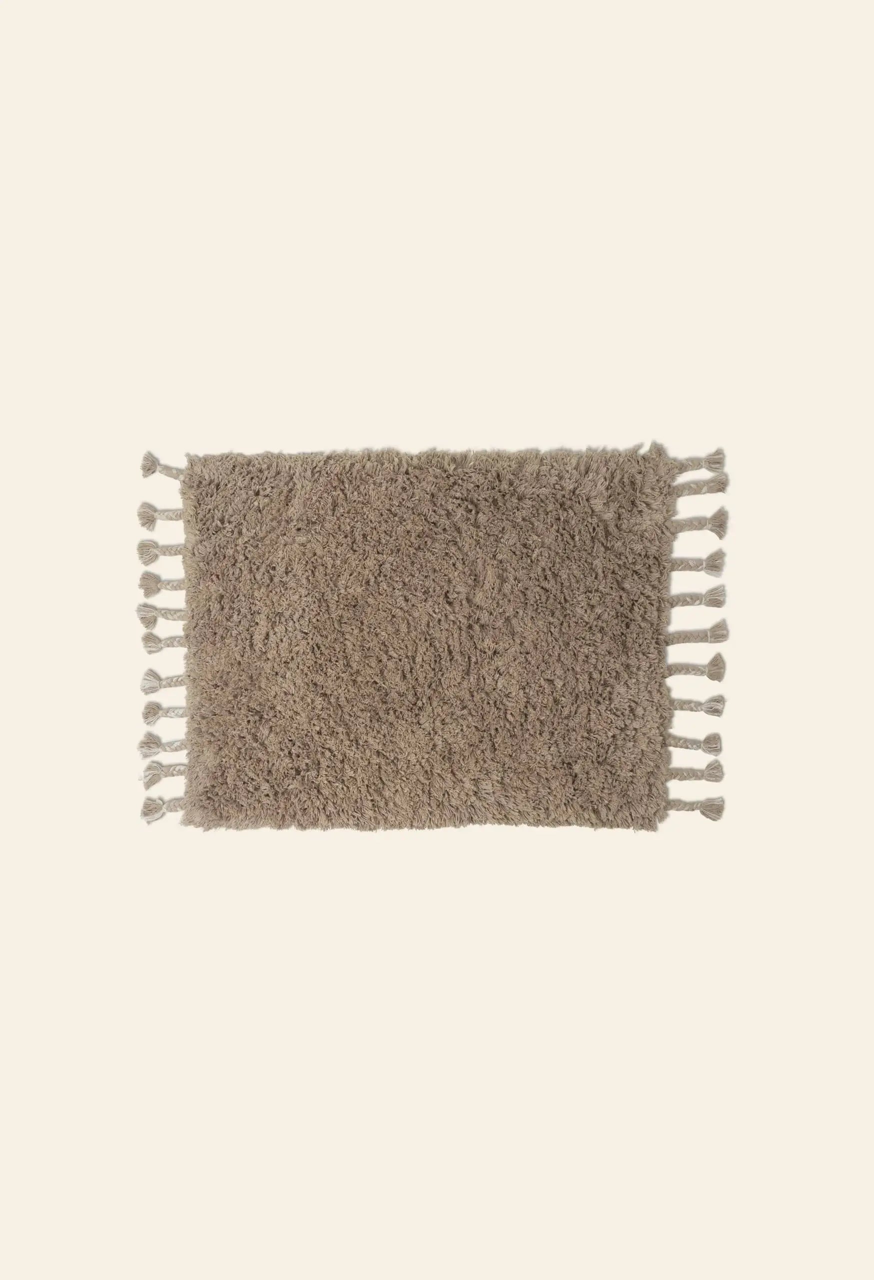 The ferm LIVING Amass Long Pile Mat by ferm LIVING is a rectangular, fluffy brown rug with tassels along the shorter edges, shown on a plain light background.