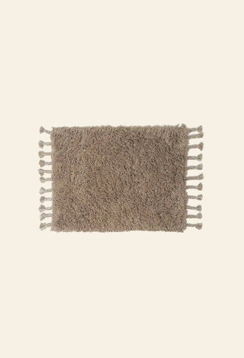 The ferm LIVING Amass Long Pile Mat by ferm LIVING is a rectangular, fluffy brown rug with tassels along the shorter edges, shown on a plain light background.