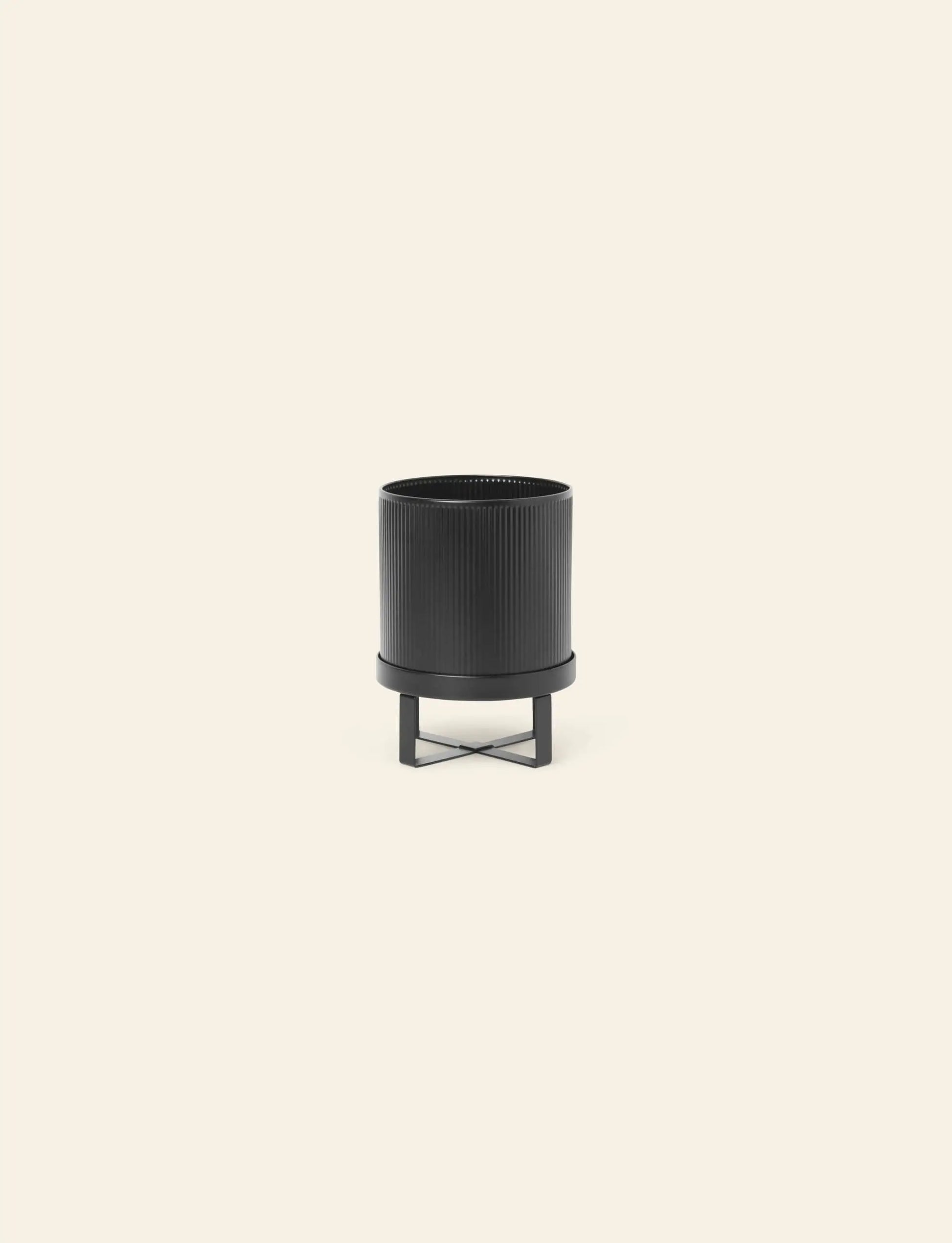 The ferm LIVING Bau Pot, Small, by ferm LIVING, features vertical ridges and sits on a matching black metal stand, its modern design inspired by Bauhaus architecture, set against a plain light beige background.