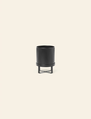 The ferm LIVING Bau Pot, Small, by ferm LIVING, features vertical ridges and sits on a matching black metal stand, its modern design inspired by Bauhaus architecture, set against a plain light beige background.