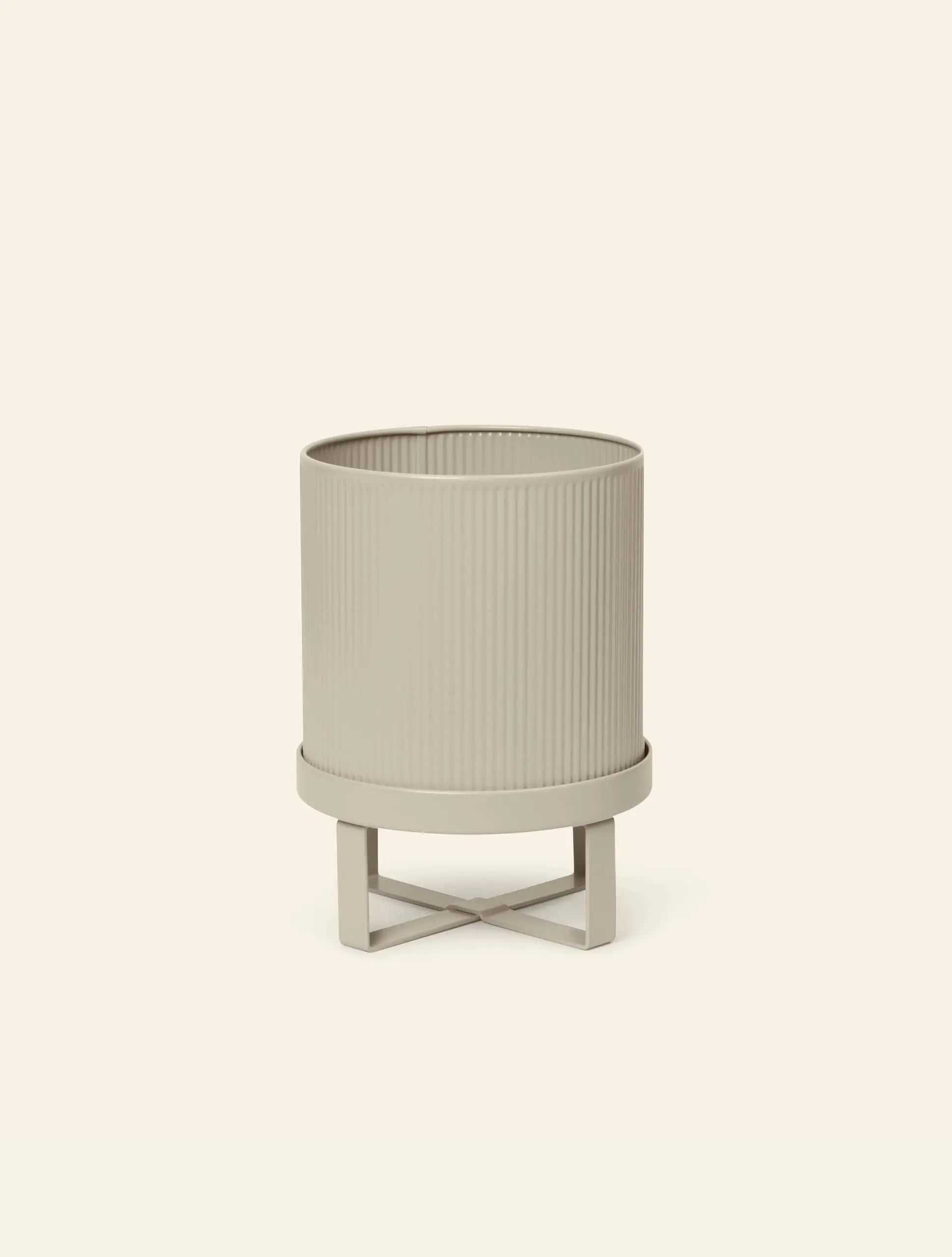 A beige, cylindrical ferm LIVING Bau Pot, Small with vertical grooves rests on a matching X-shaped stand against an off-white background, echoing the clean lines of Bauhaus architecture.