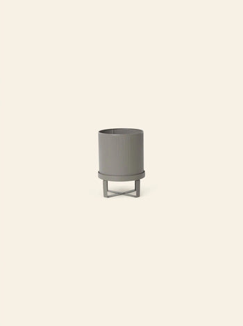 The ferm LIVING Bau Pot, Small, is a gray, round, ribbed modern pot with a matching stand inspired by Bauhaus architecture, shown against a plain light beige background.