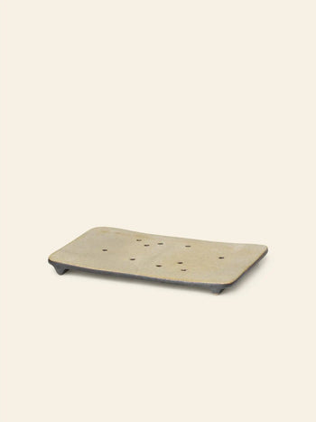 The ferm LIVING Bon Accessories Soap Tray is a rectangular beige porcelain tray with drainage holes and short feet, adding elegance to your bathroom. Displayed on a plain light background.
