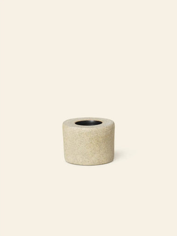 The ferm LIVING Bon Accessories Toothbrush Holder features a small, cylindrical beige stone design with a central round opening, offering sleek style from ferm LIVING against a plain light background.