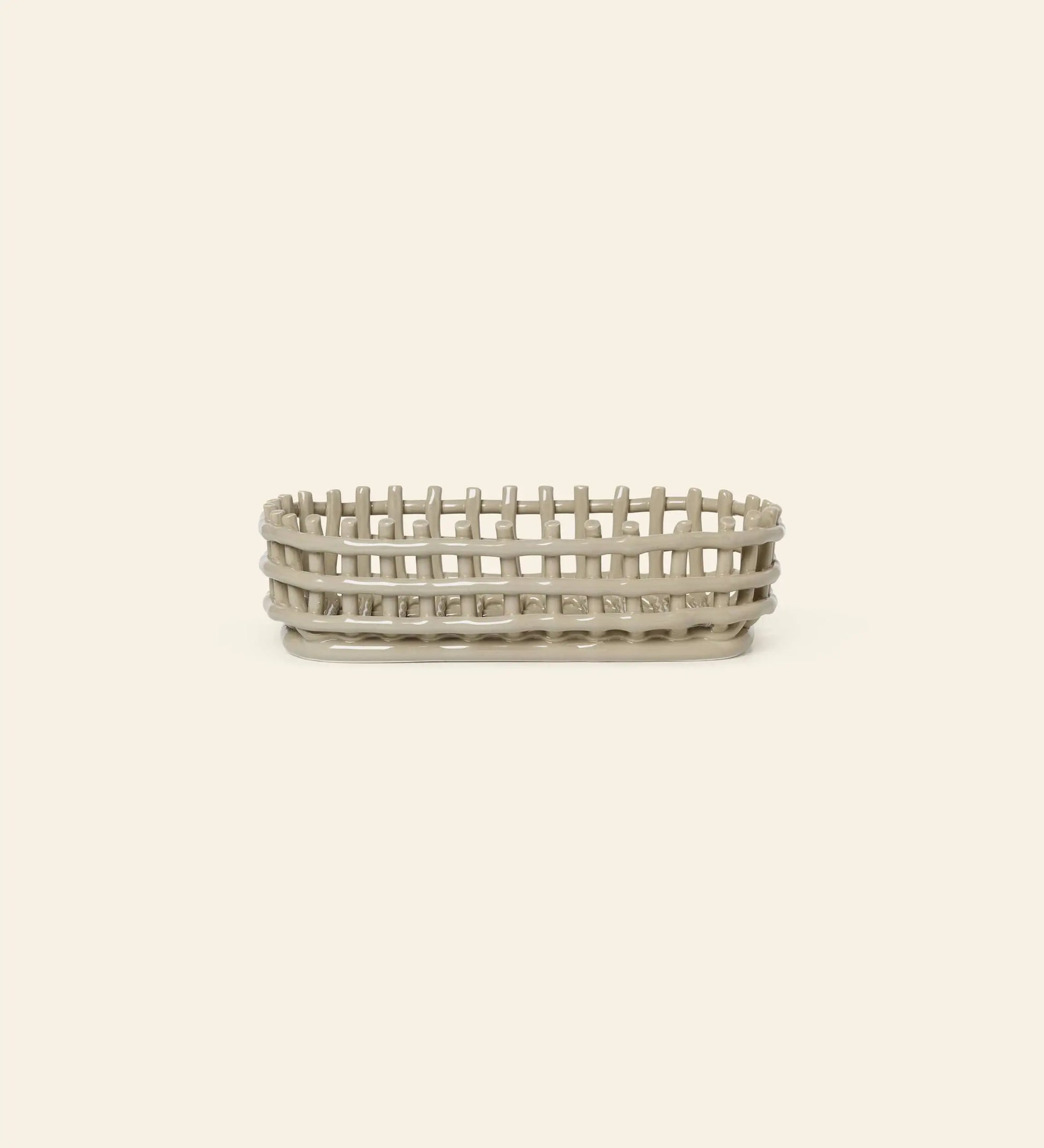 The ferm LIVING Ceramic Basket Oval by ferm LIVING is a contemporary, oval-shaped basket with an open-weave design and solid base, crafted in light beige ceramic, shown against a plain off-white background.