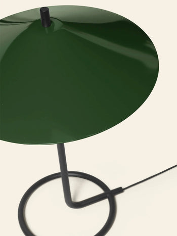 The ferm LIVING Filo Table Lamp by ferm LIVING showcases a glossy dark green, cone-shaped powder coated iron shade and a black circular base with a black power cord, ideal for modern homes.
