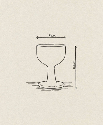 A line drawing of the ferm LIVING Floccula Wine Glass, shaped like a balloon wine glass with a wide base, labeled 9 cm wide and 11.5 cm tall, is set against a textured off-white paper background.