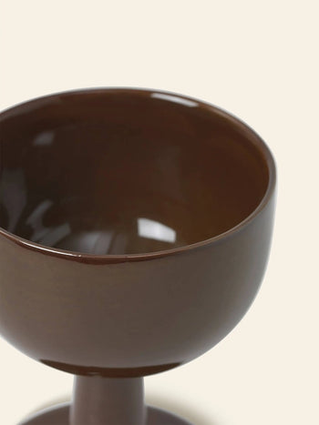 Close-up of the ferm LIVING Floccula Wine Glass by ferm LIVING, featuring a glossy dark brown ceramic finish. Only the upper half and part of the stem are shown against a simple light-colored background.