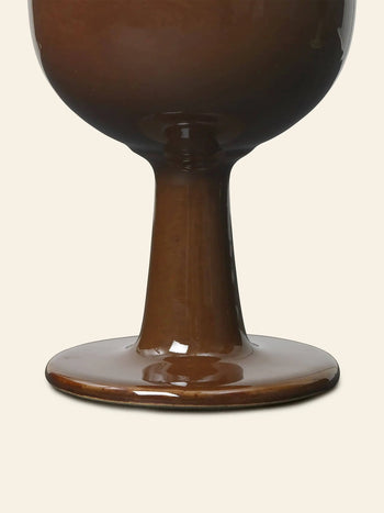 Close-up of the base and stem of the glossy brown ferm LIVING Floccula Wine Glass, set against a plain, light beige background.