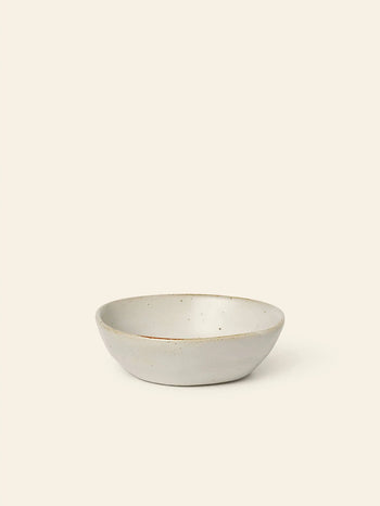 The ferm LIVING Flow Porcelain Bowl, Small, features a minimalist, off-white design and shallow round shape—an elegant piece of artisanal tableware from the renowned brand ferm LIVING.