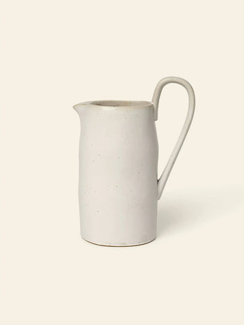 The ferm LIVING Flow Jug by ferm LIVING is a simple off-white ceramic piece with organic curves, a curved handle, and narrow spout—ideal for minimalist kitchen decor.