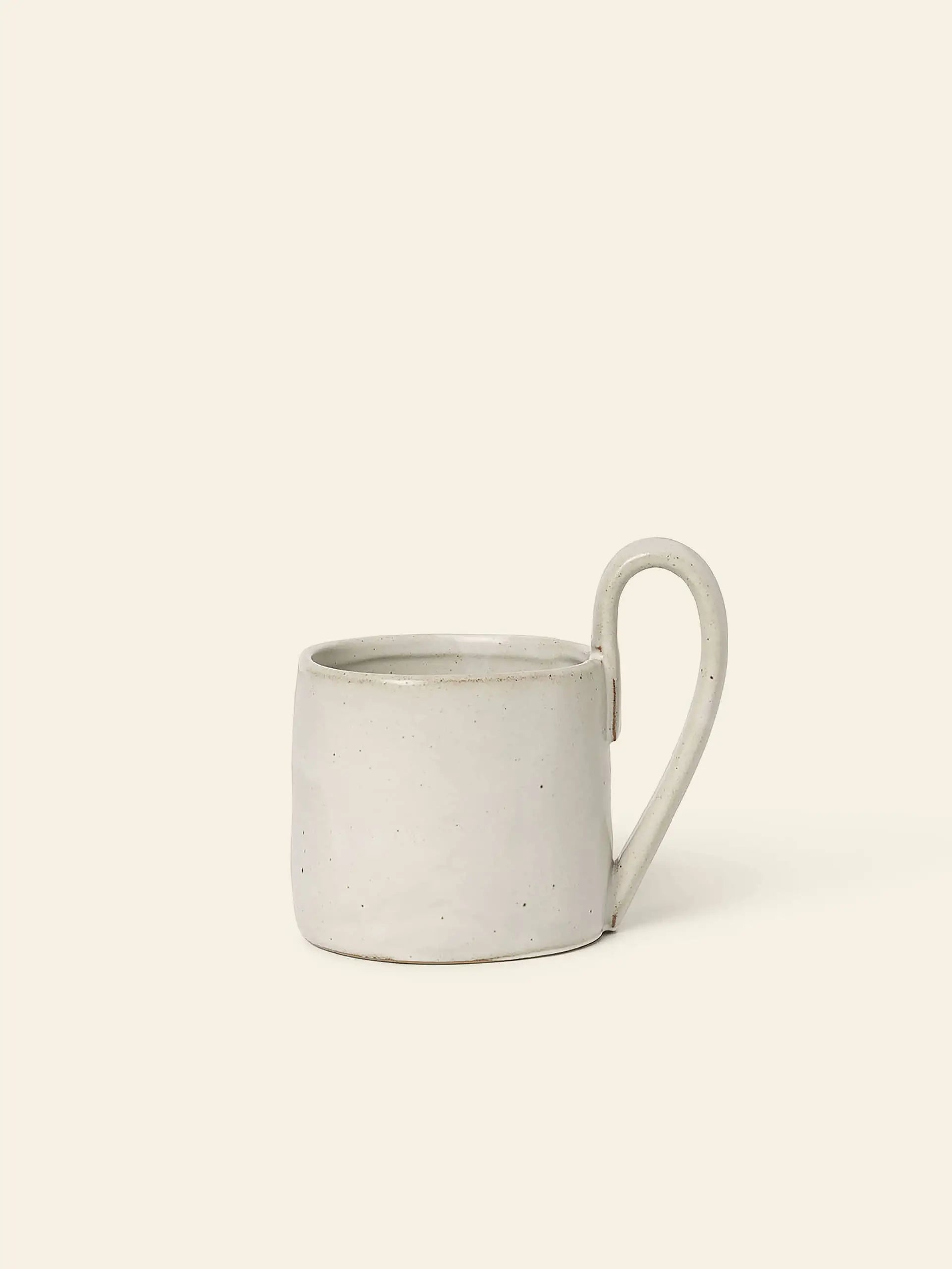 The ferm LIVING Flow Mug boasts a minimalist design with a light gray matte finish, subtle speckled texture, and large rounded handle. Its soft curves and organic style make it perfect for calm, serene spaces.