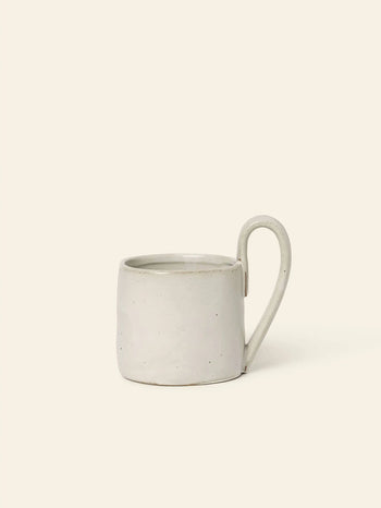 The ferm LIVING Flow Mug boasts a minimalist design with a light gray matte finish, subtle speckled texture, and large rounded handle. Its soft curves and organic style make it perfect for calm, serene spaces.