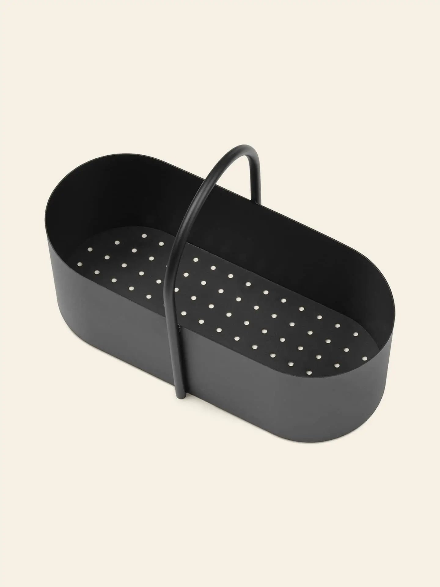 The ferm LIVING Grib Toolbox by ferm LIVING is a black, oval metal basket with a slim handle and perforated bottom, ideal for draining or steaming. The background is plain light beige.