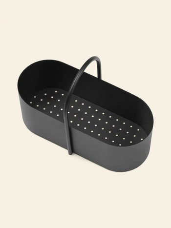 The ferm LIVING Grib Toolbox by ferm LIVING is a black, oval metal basket with a slim handle and perforated bottom, ideal for draining or steaming. The background is plain light beige.