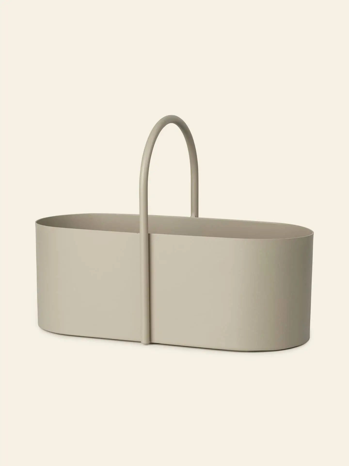 The ferm LIVING Grib Toolbox is a minimalist, oval-shaped beige basket with a slim design and tall curved handle, ideal for stylishly organizing stationery or other items against a light background.