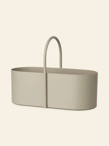The ferm LIVING Grib Toolbox is a minimalist, oval-shaped beige basket with a slim design and tall curved handle, ideal for stylishly organizing stationery or other items against a light background.