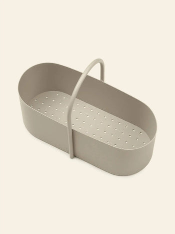 The ferm LIVING Grib Toolbox by ferm LIVING, featuring an oval shape, beige color, plastic build, slim design with small bottom holes and a curved top handle, is shown on a plain light background.